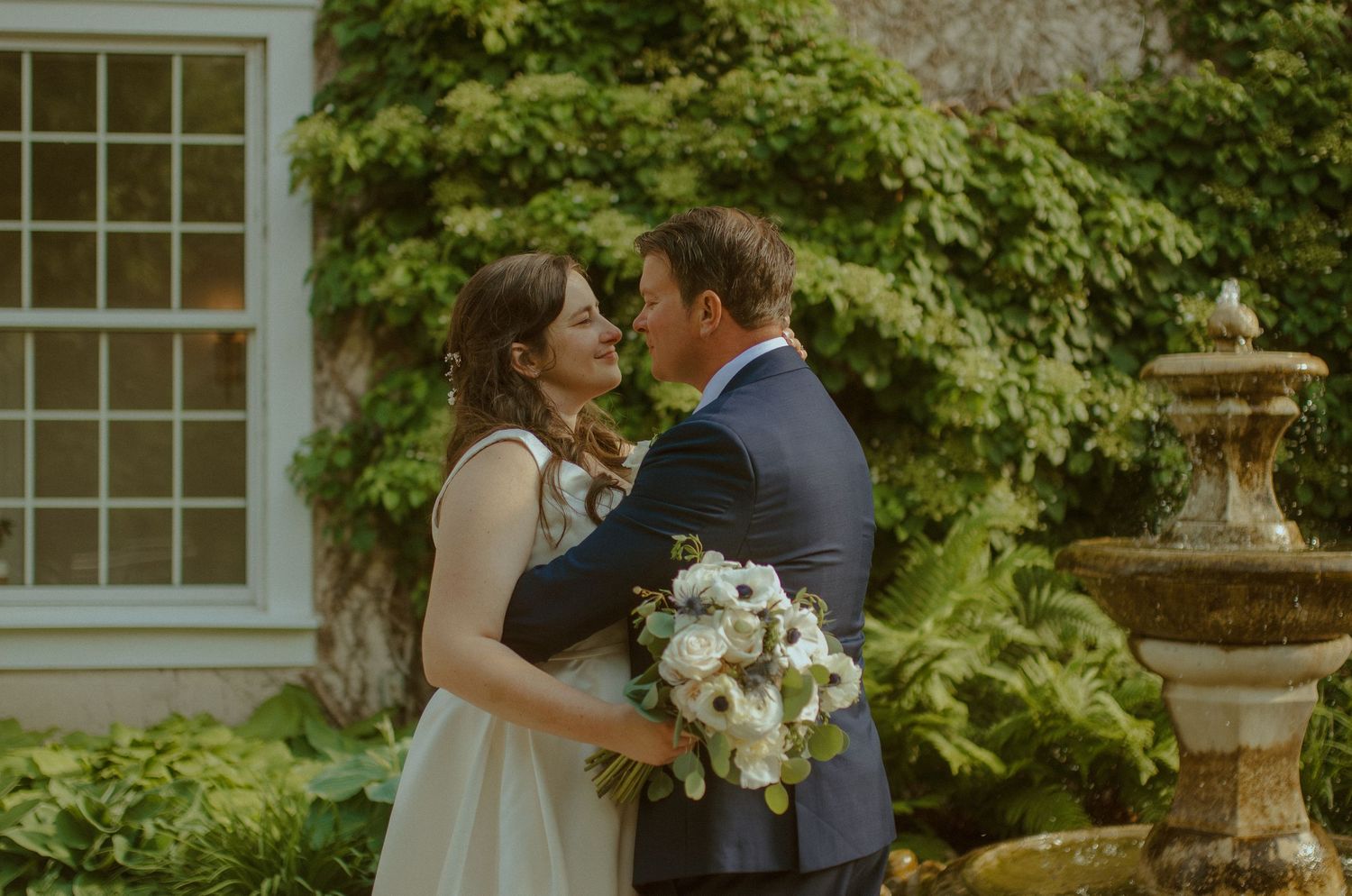 Happy newlyweds embrace in front of lush green garden foliage during their wedding celebration.