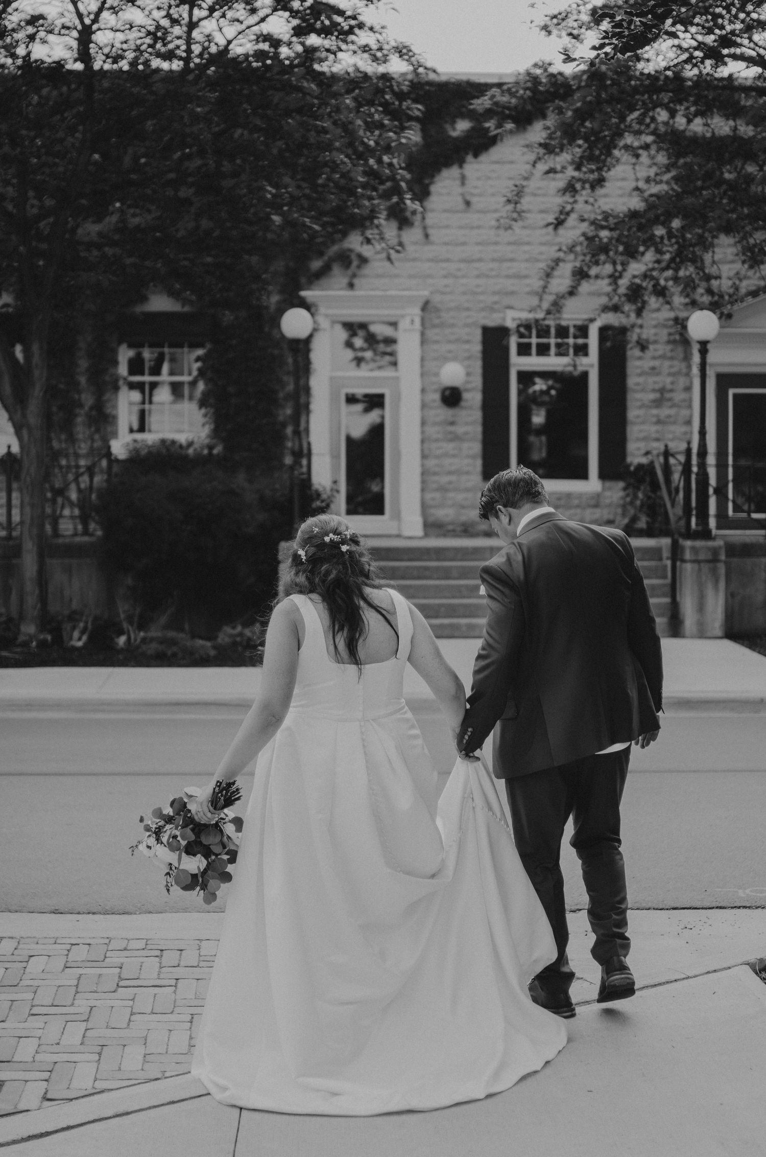 Black and white photo series of a couple in wedding attire walking along a brick pathway.