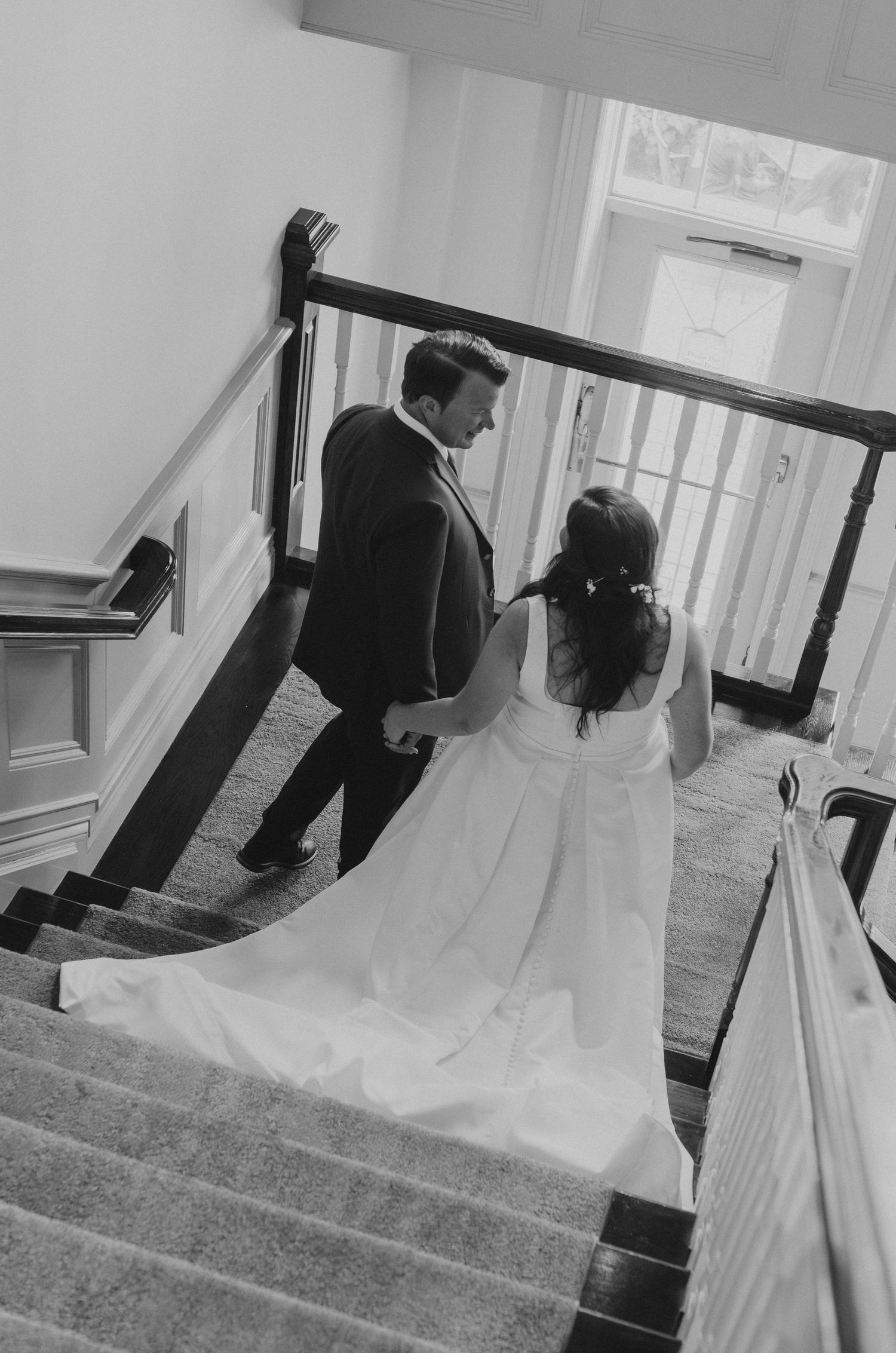 A couple descends an elegant staircase, with the bride's white dress trailing behind them on the wooden steps.