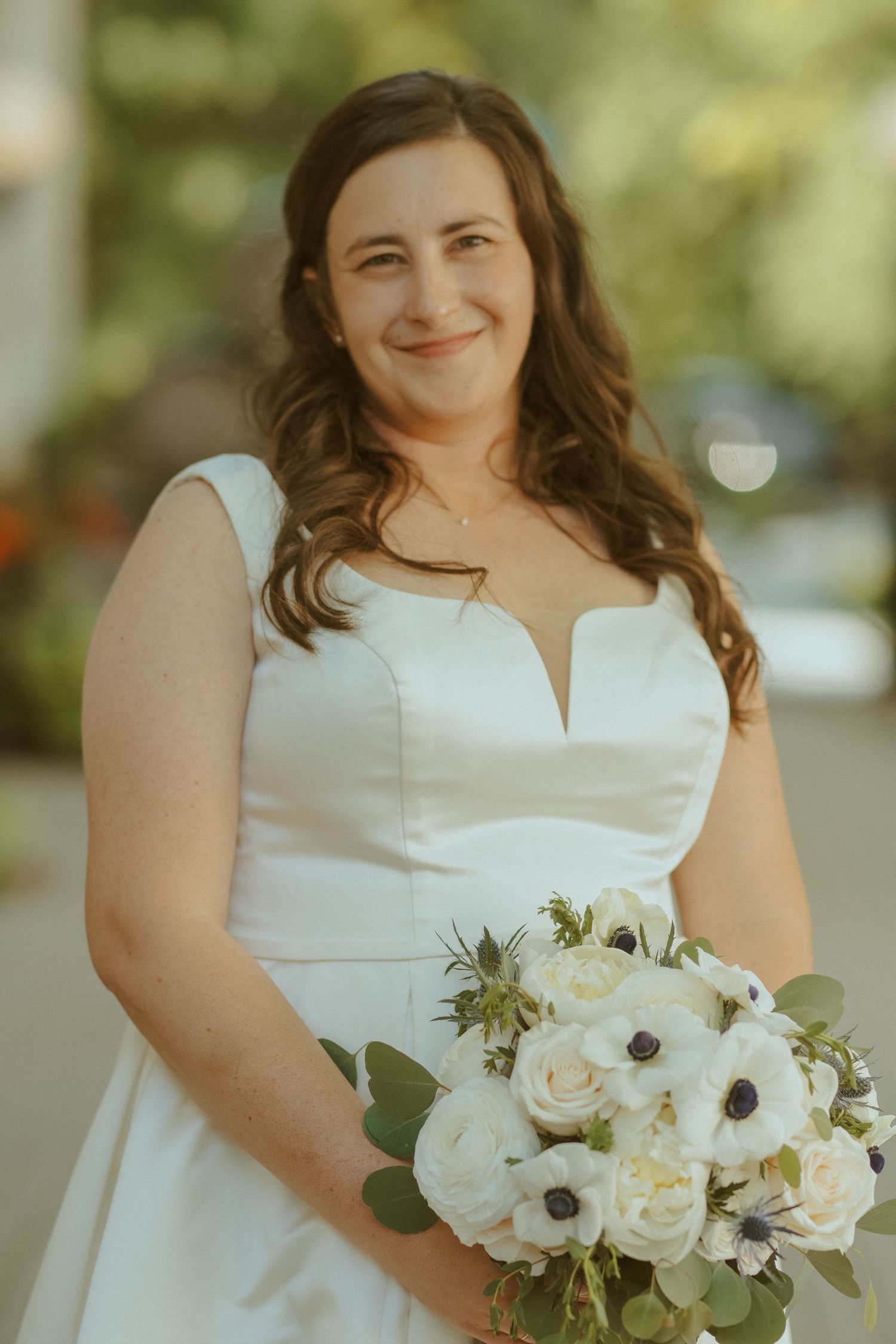 Beautiful bridal bouquet featuring white anemones and roses against a white wedding dress.
