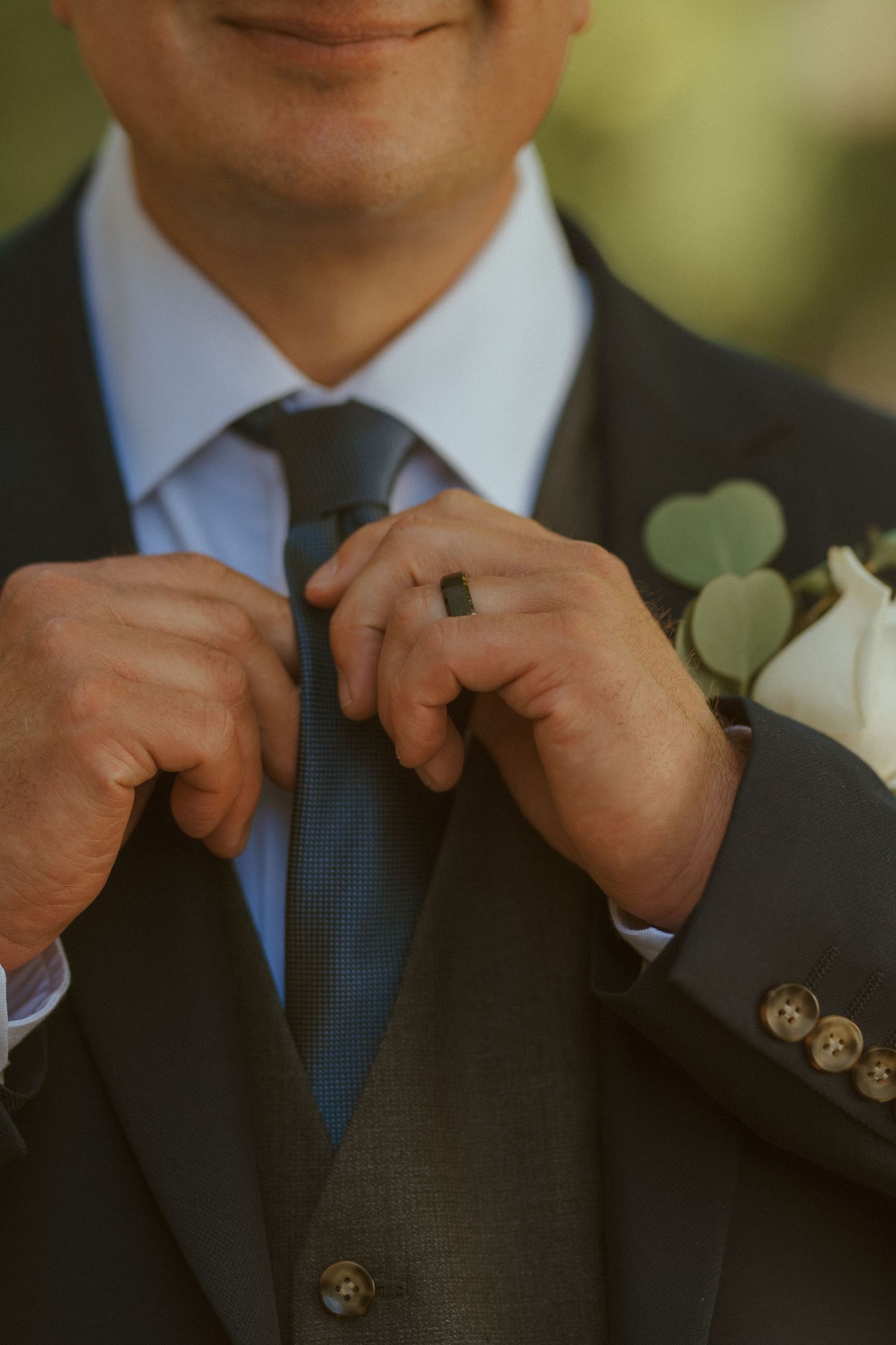 Close-up of hands adjusting a navy blue tie and boutonniere on a formal suit.