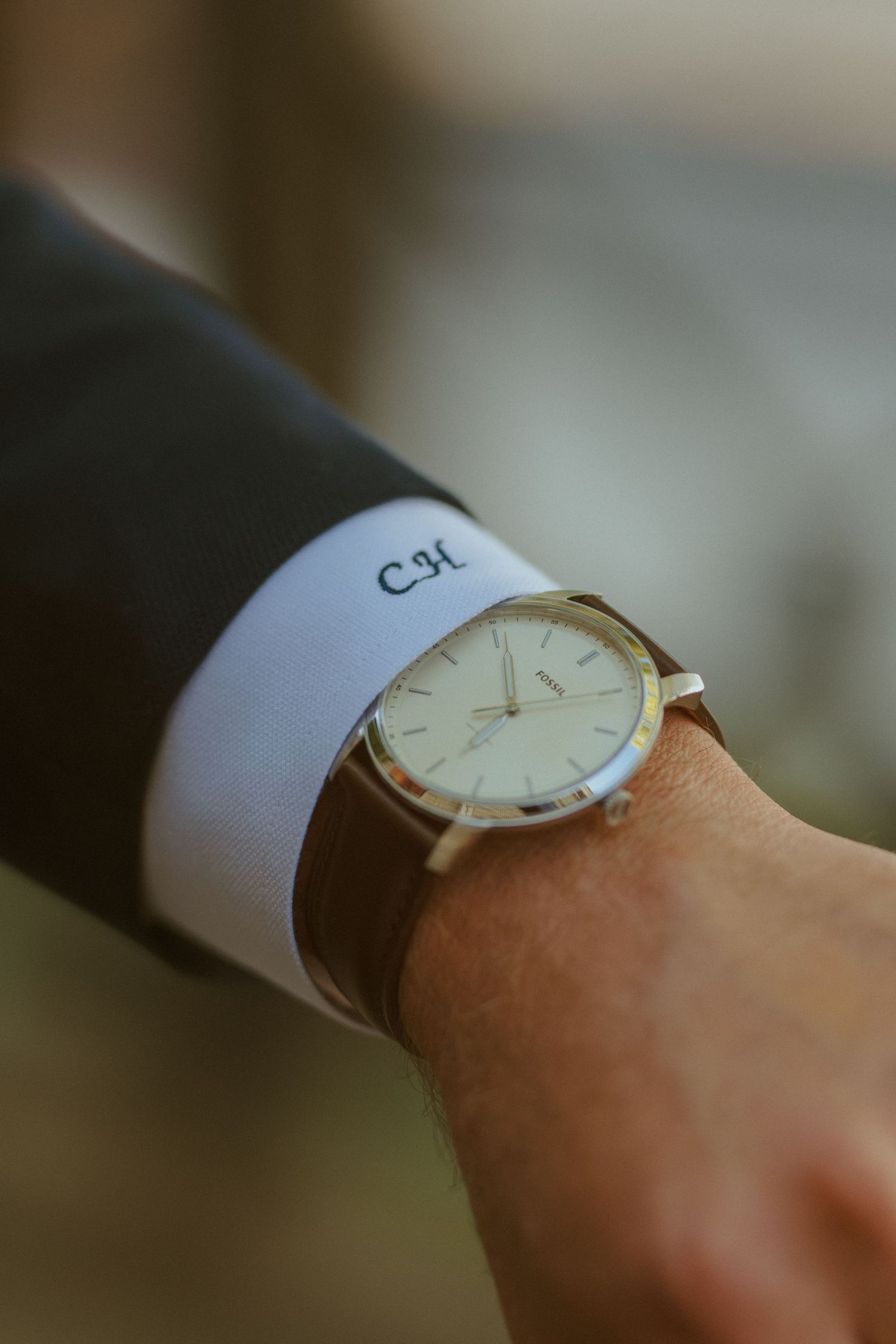 An elegant wristwatch with monogrammed 'CSK' cuff displayed on a suited arm.