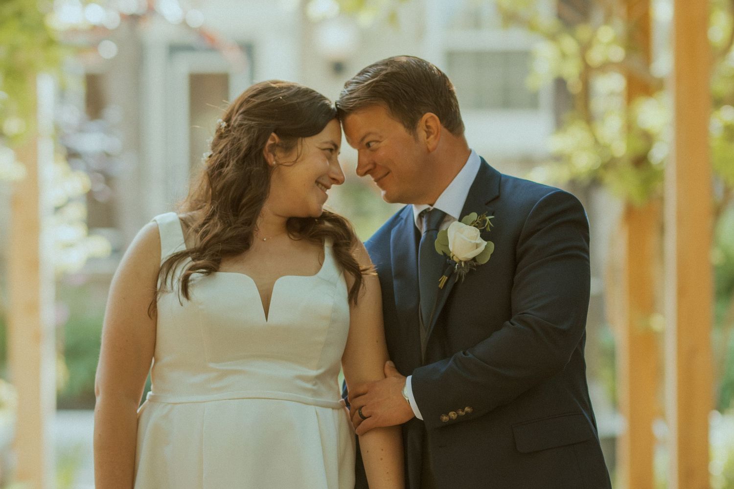 A romantic couple shares a tender moment in wedding attire during golden hour beneath a wooden pergola.
