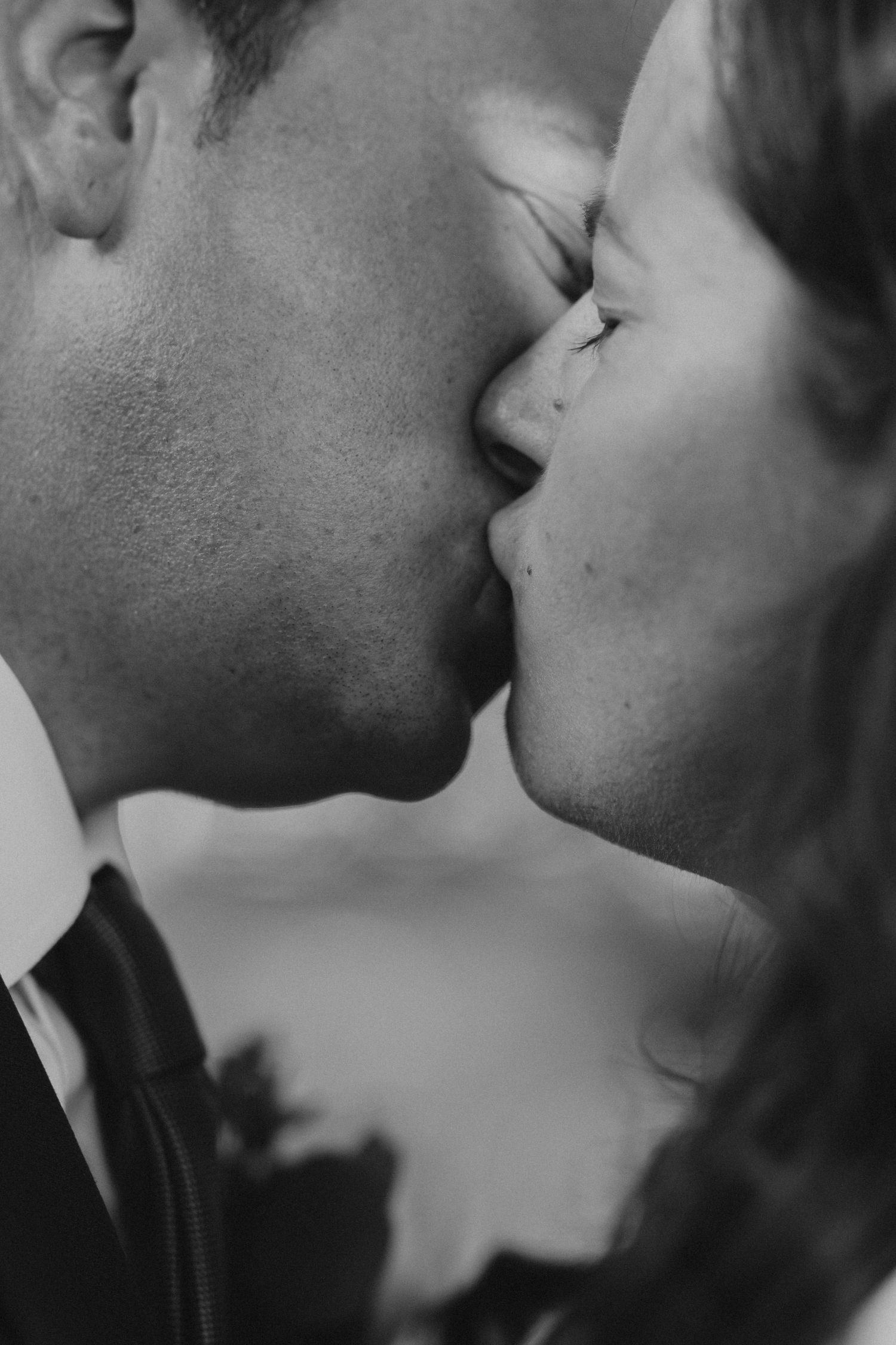 Close-up black and white portrait of a tender kiss between newlyweds.