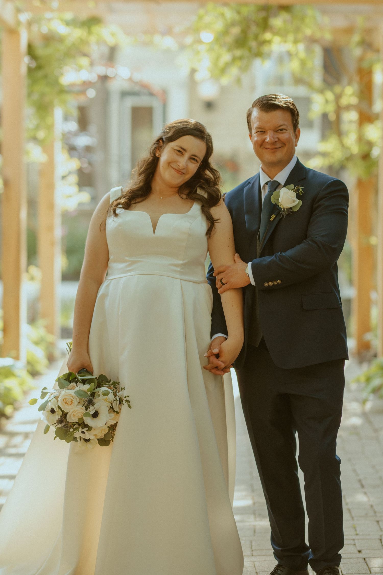 A couple poses together during their wedding, with the bride in a white gown holding a delicate bouquet.
