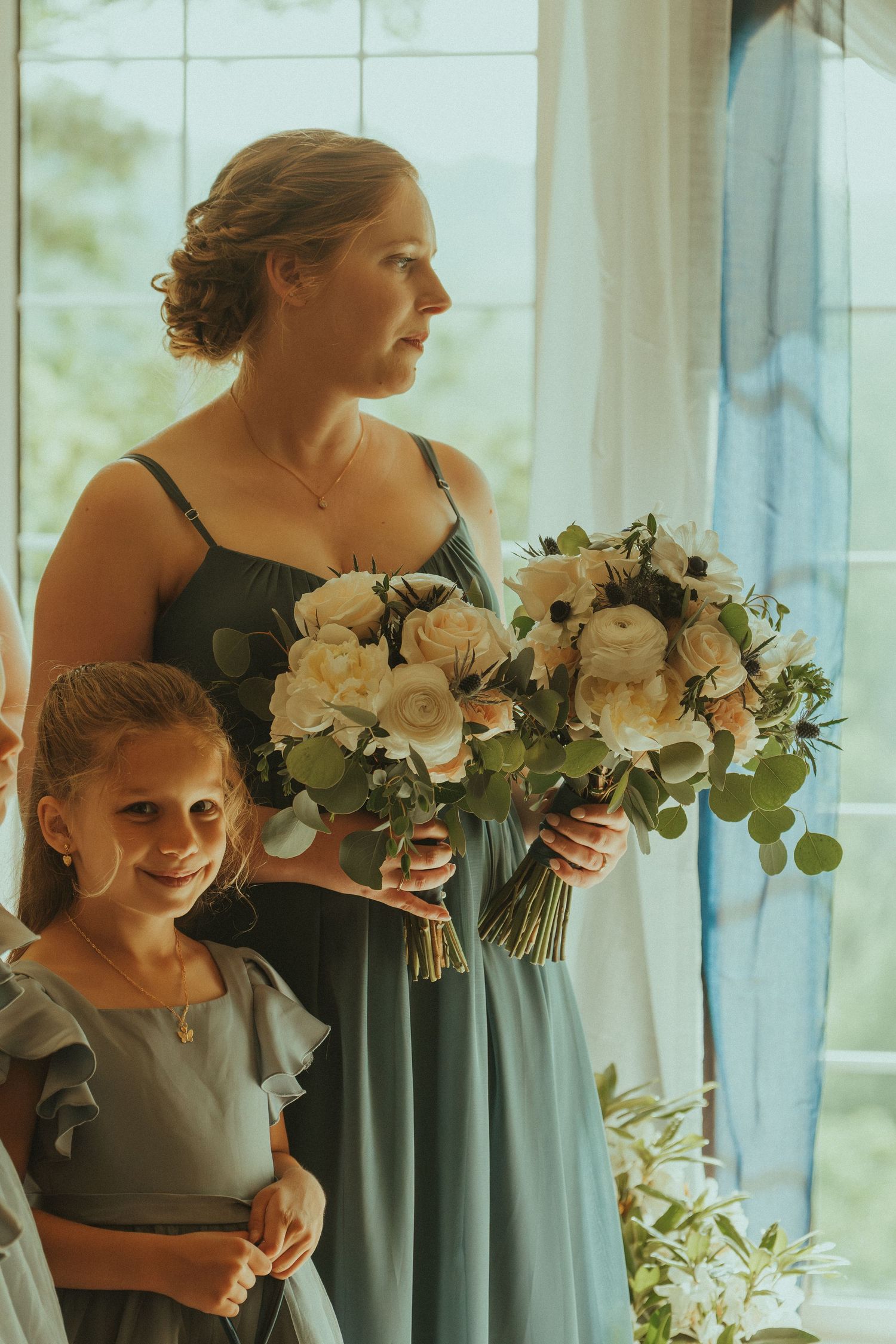 Wedding party holding elegant white floral bouquets by sunlit windows.