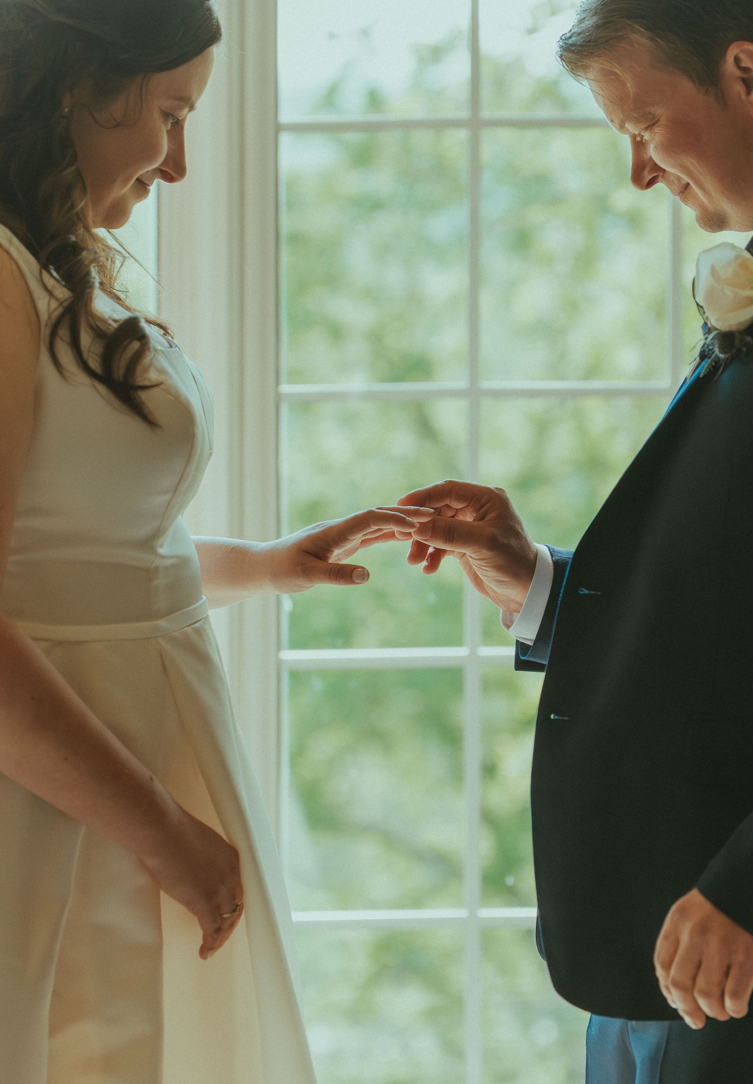 Intimate candid moment between wedding couple against bright window light.