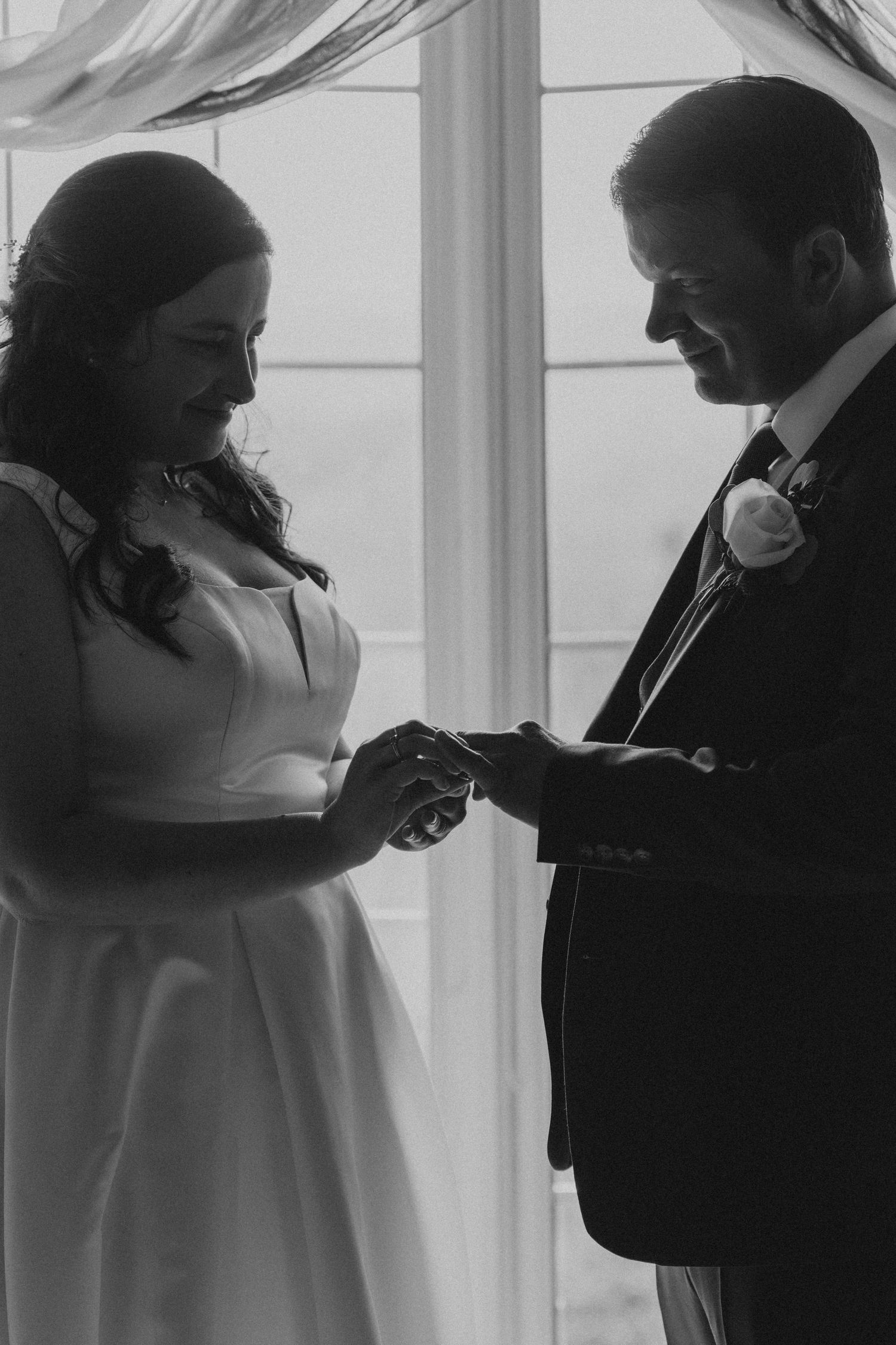 Silhouetted wedding couple sharing an intimate moment by large windows.