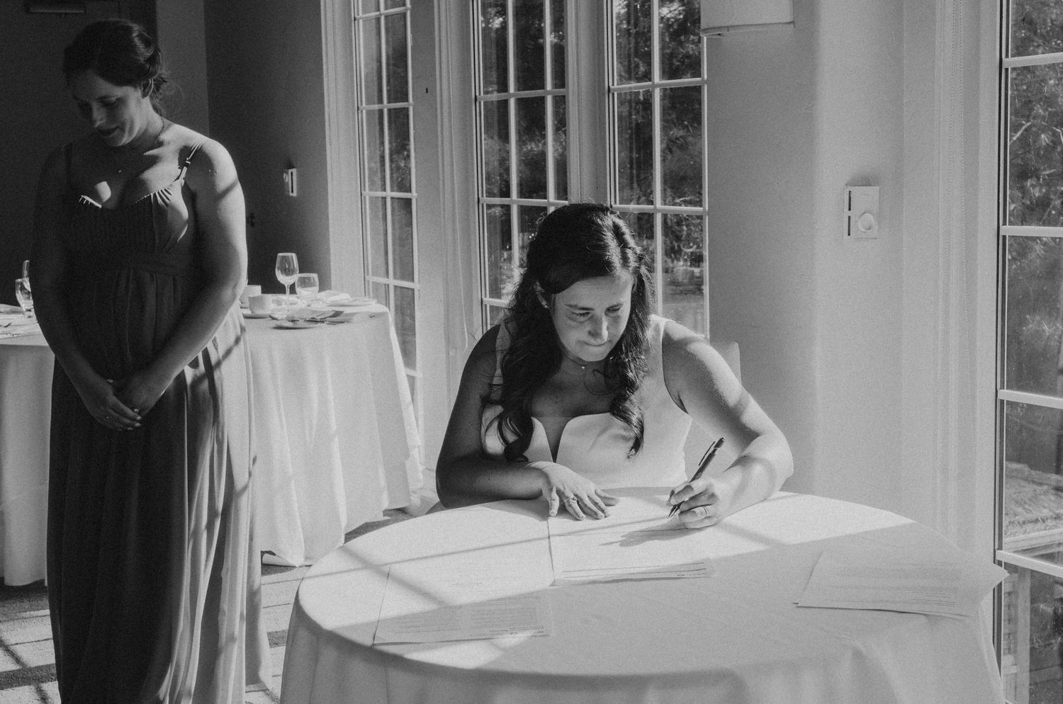 Black and white image of wedding guests signing documents at a reception.