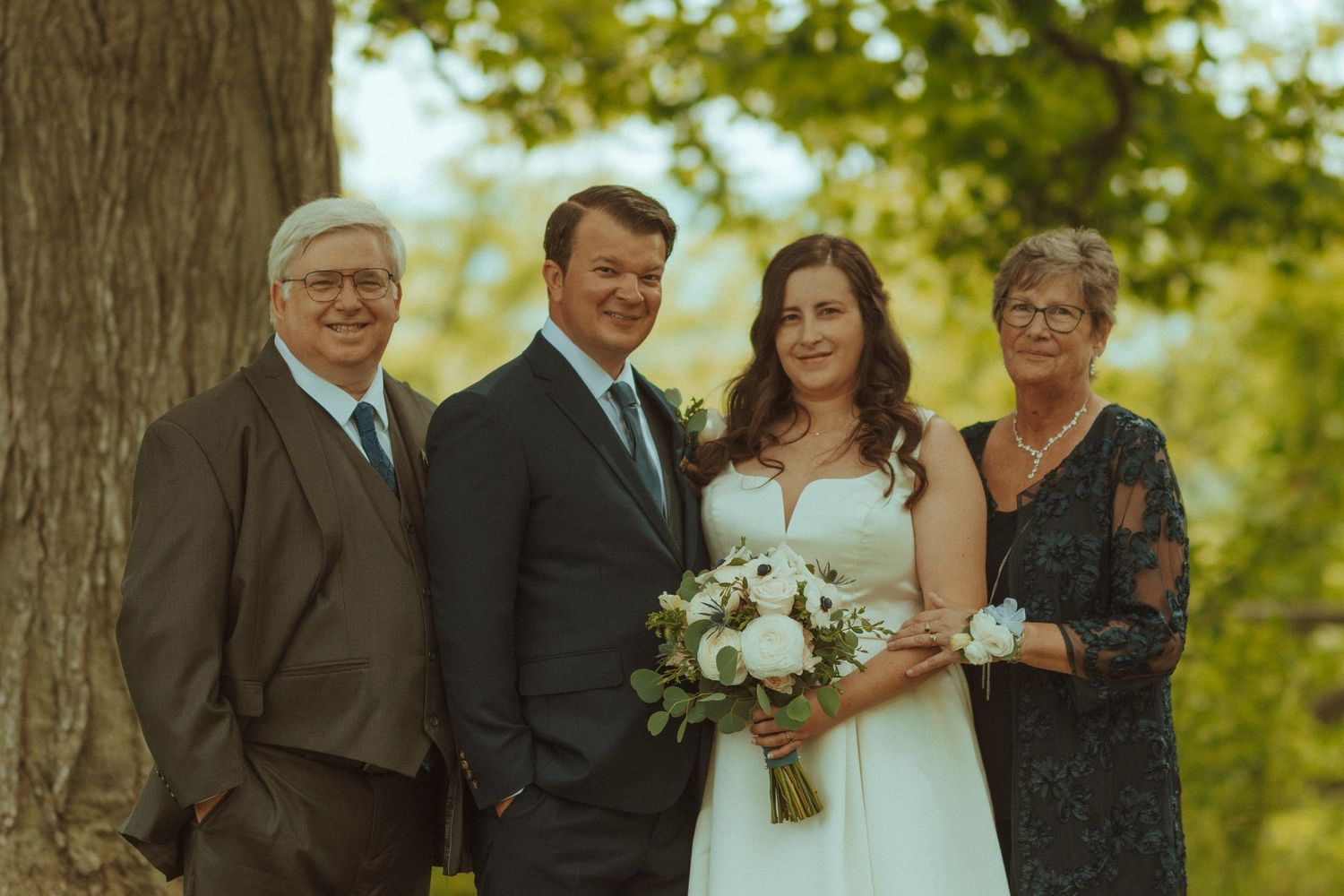 Wedding party gathered outdoors for formal portraits under trees.