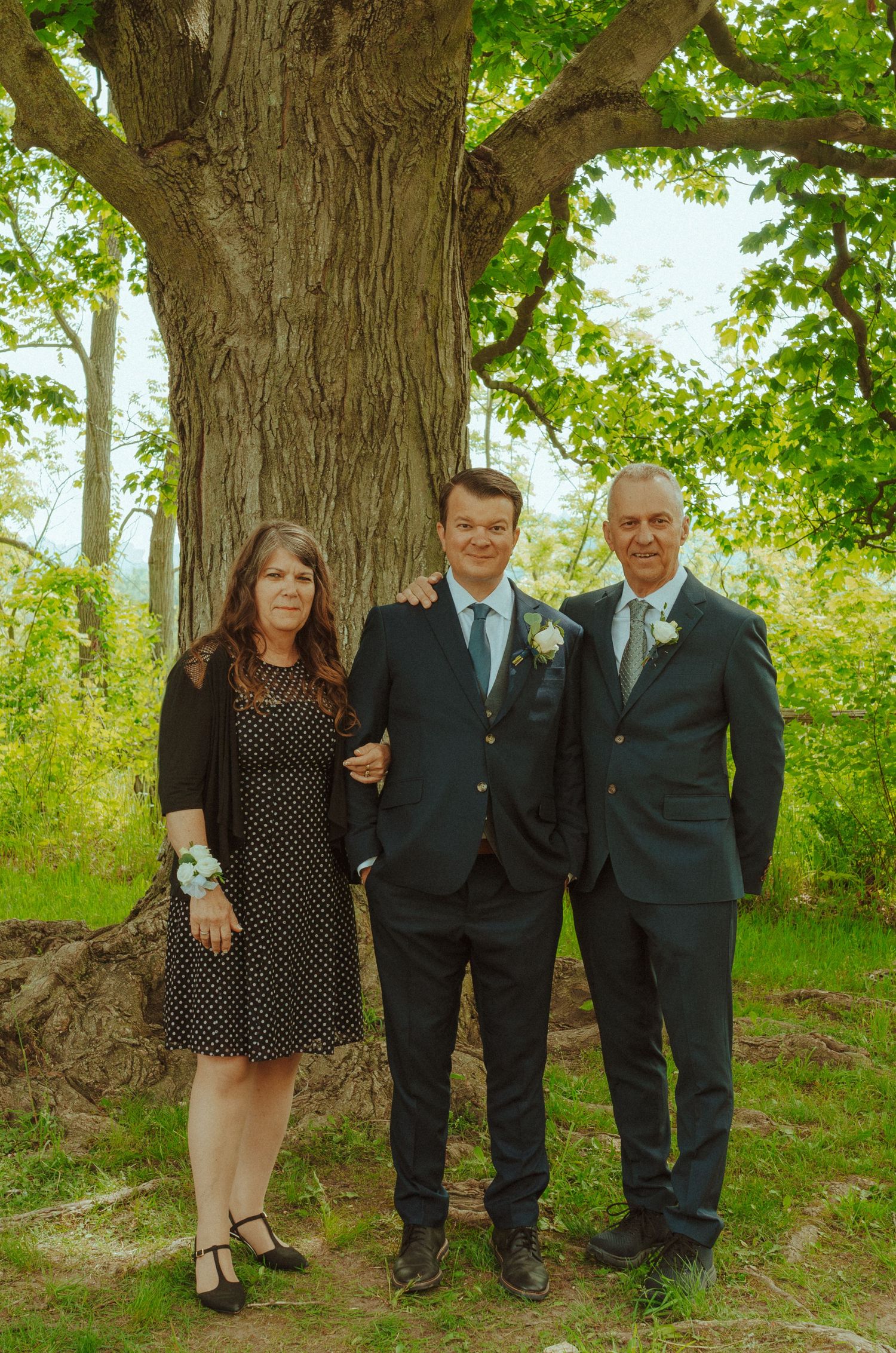 Small group poses together under a large tree during outdoor wedding festivities.