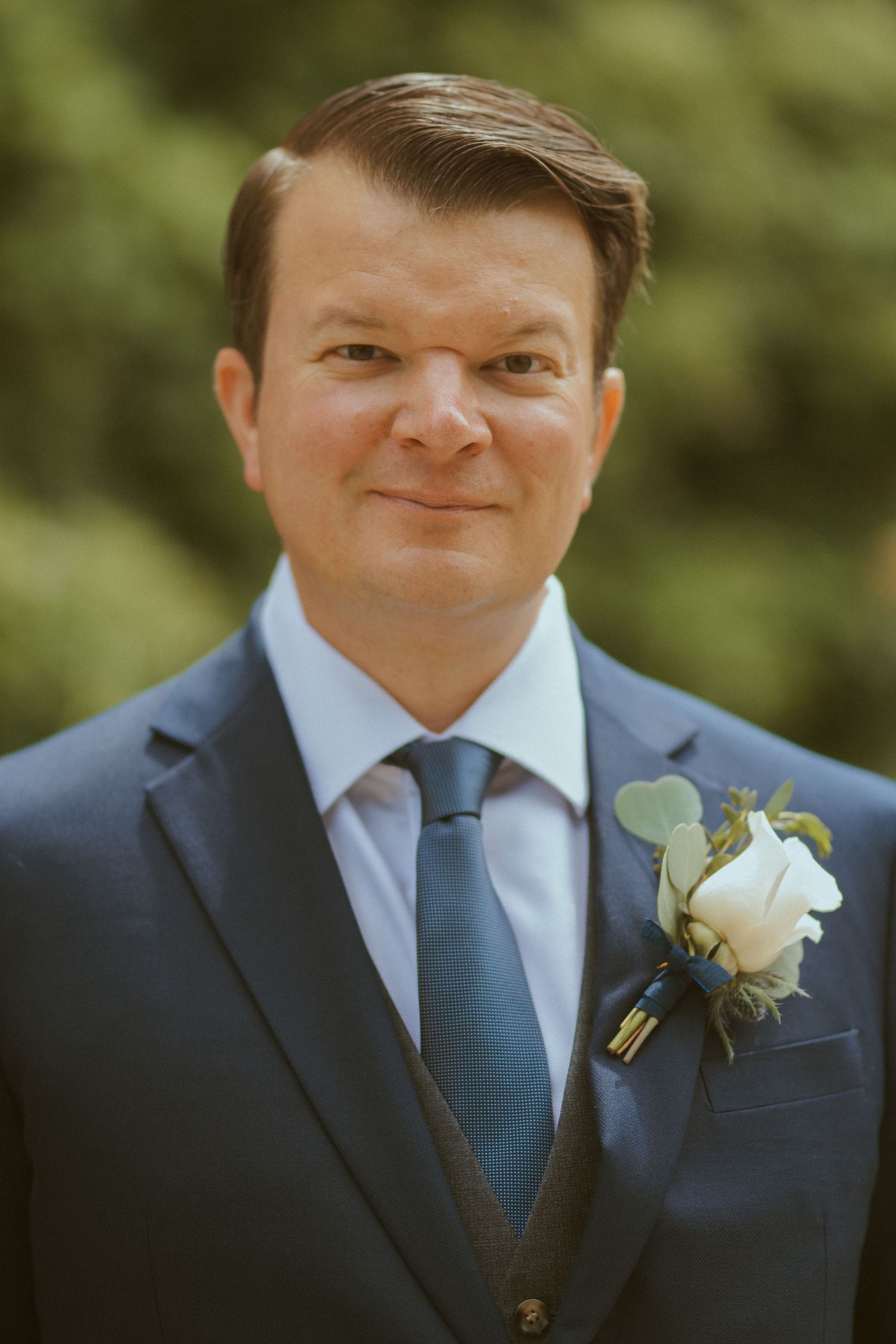 Close-up portrait series of a groom wearing a navy suit with white boutonniere.