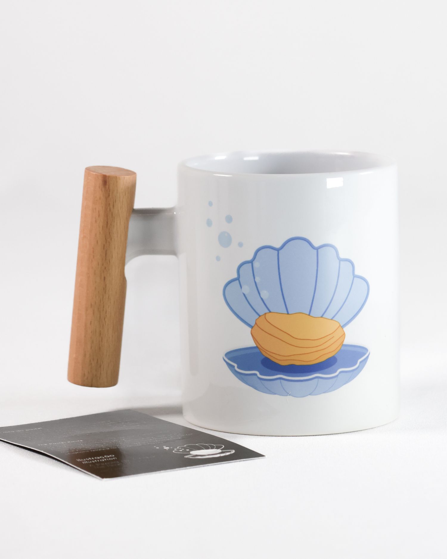 White ceramic mug with blue seashell illustration and wooden handle.