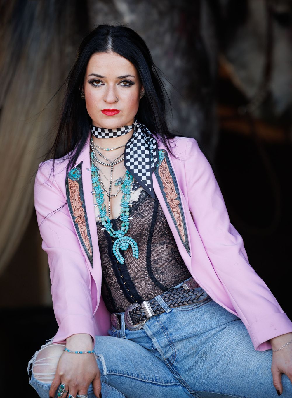 Alternative fashion model wearing pink blazer, black mesh top, turquoise accessories and denim in edgy studio photoshoot.