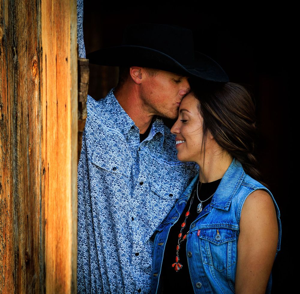 A romantic western-style couple sharing an intimate moment against a rustic wooden backdrop.