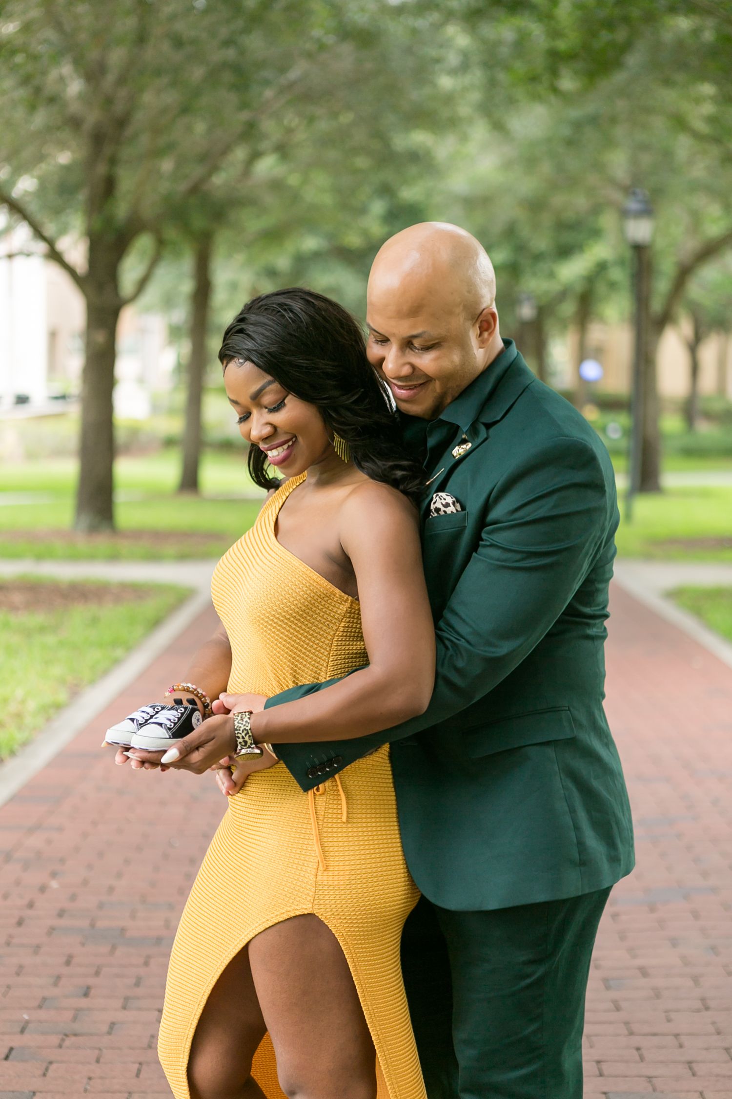A couple shares a joyful embrace on a brick path surrounded by green trees in Winter Park, Orlando Maternity Photography, Sanford Maternity