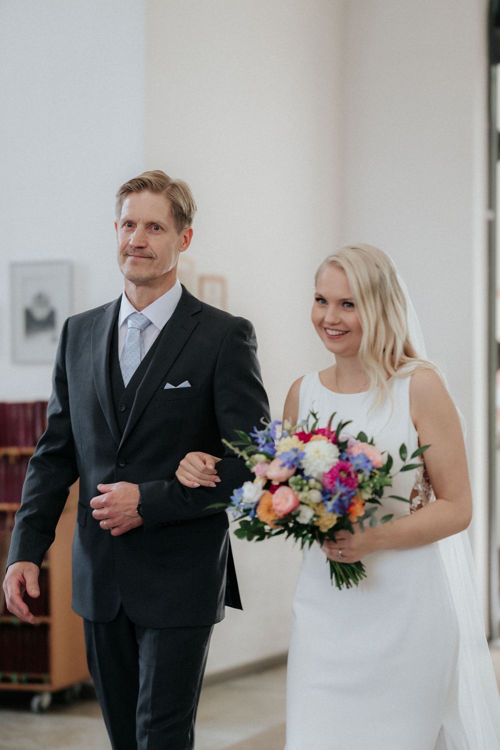 A joyful wedding moment captured as the bride holds a colorful floral bouquet while walking with her escort in church.