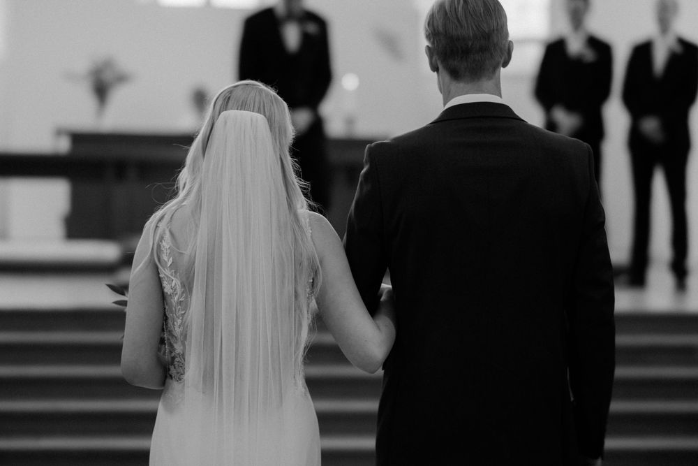 Wedding couple faces church altar while guests and clergy stand behind them during traditional ceremony.