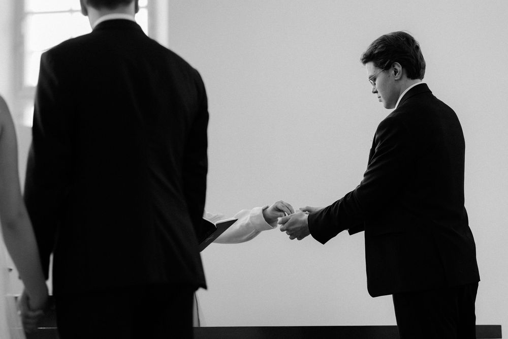 Two figures in dark suits shaking hands in a dramatic black and white business gesture against a light background.