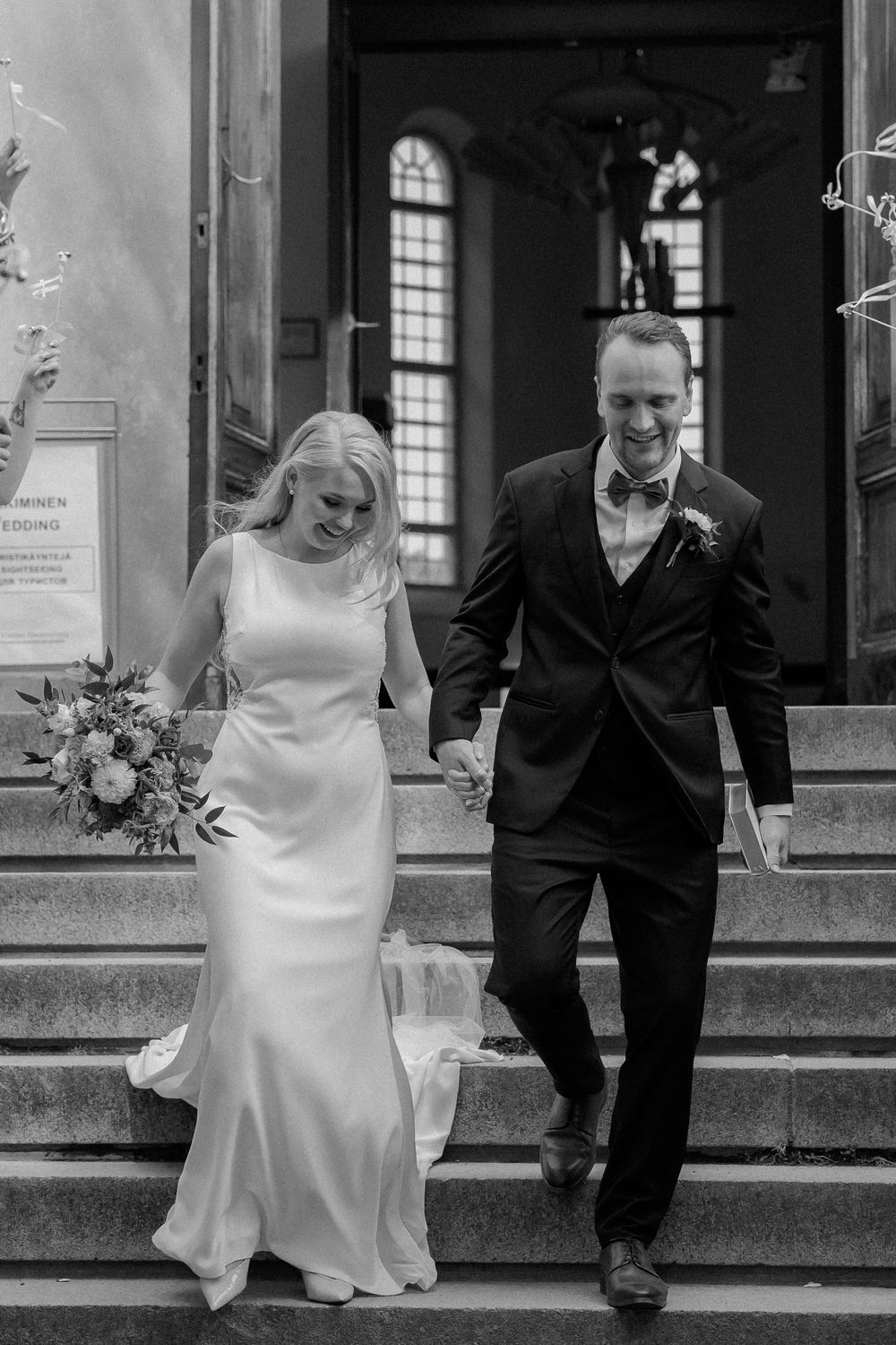 A couple in wedding attire share a joyful moment running together outside a traditional building.