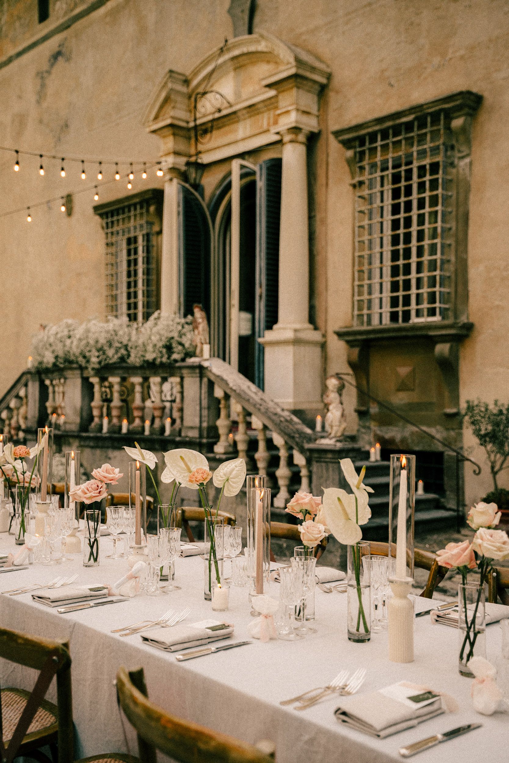 Elegant wedding reception table settings with vintage glass bottles and floral centerpieces in a rustic architectural space.