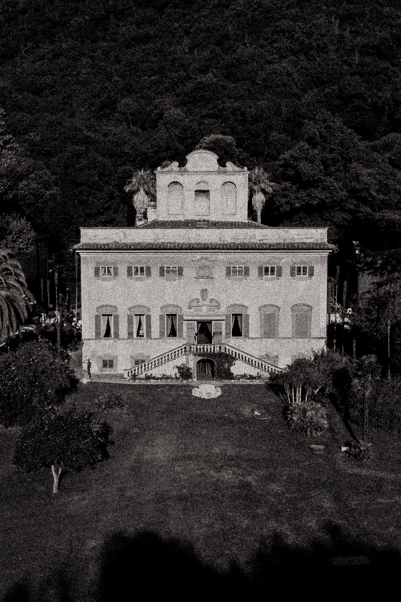 Historic Italian villa with white facade and symmetrical architecture nestled among dark trees on a hilltop at dusk.