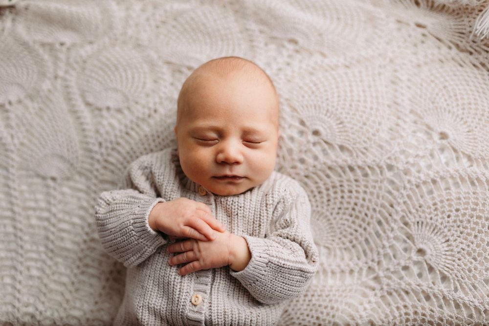 Sweet newborn baby in grey onesie lying on textured white blanket.