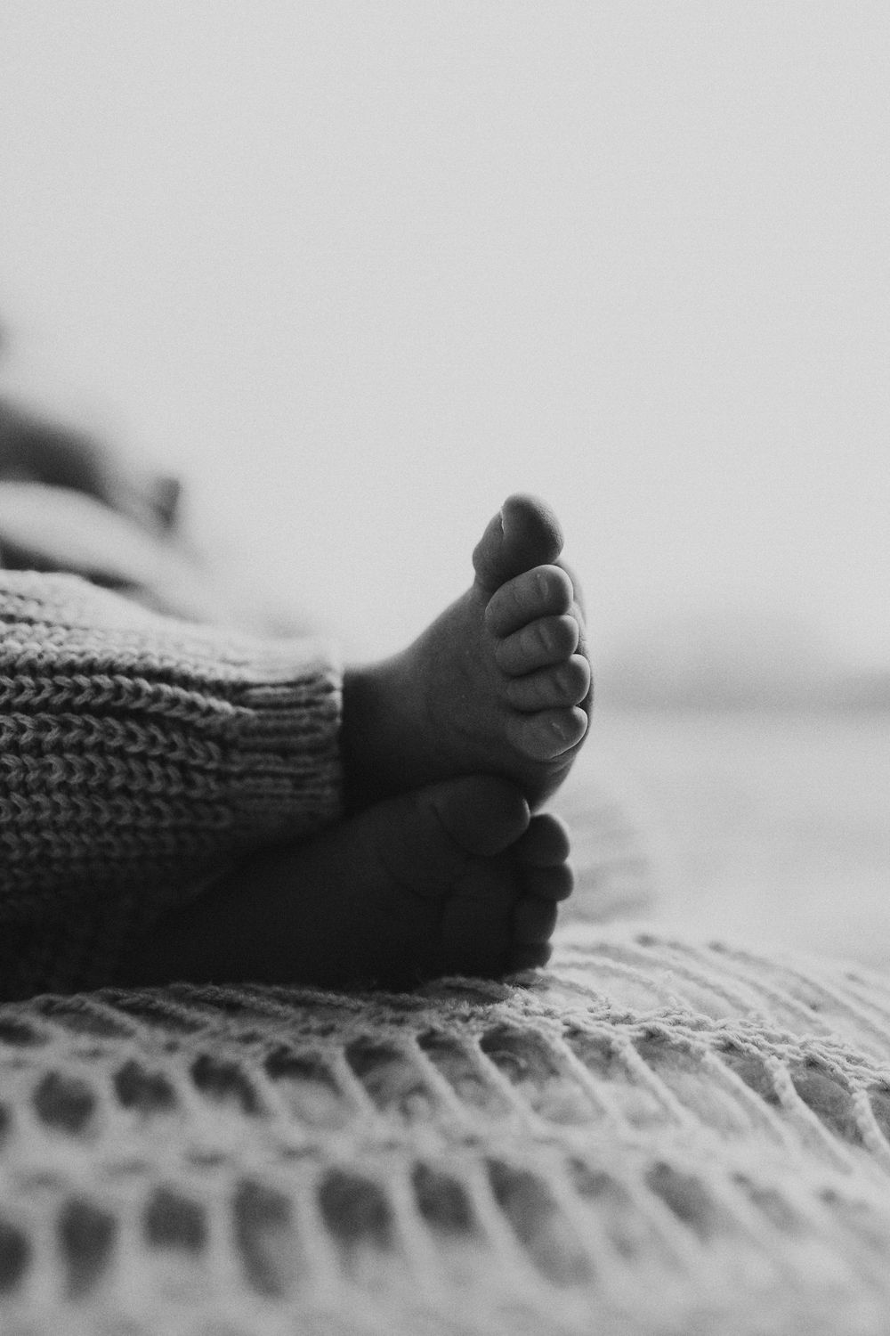 Close-up black and white shot of tiny baby feet resting on a textured knit blanket.