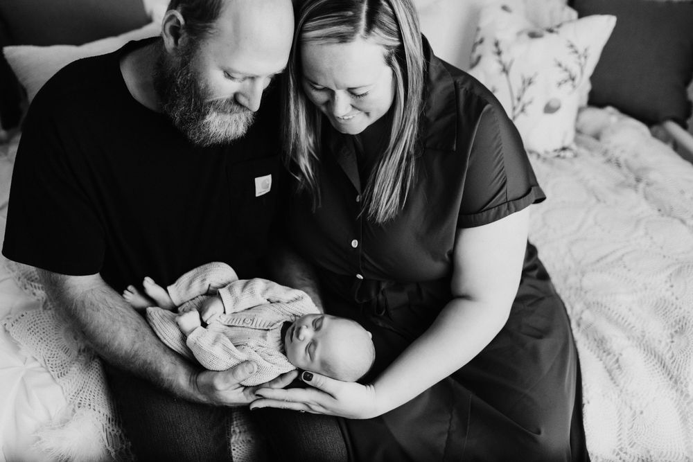 Black and white intimate photo of parents tenderly cradling their newborn.