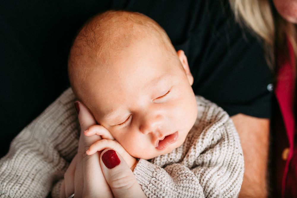 Baby sleeping peacefully in a cozy white knit sweater against a dark background.