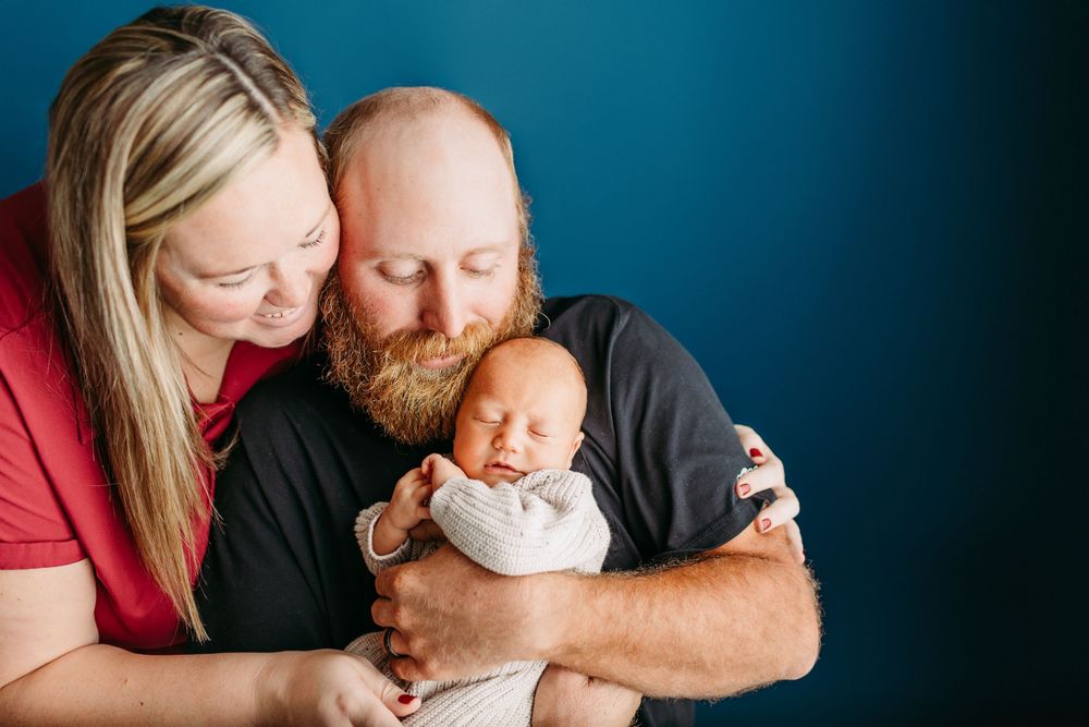 A series of four intimate family portrait photos showing tender moments between parents and their newborn baby against dark backgrounds.