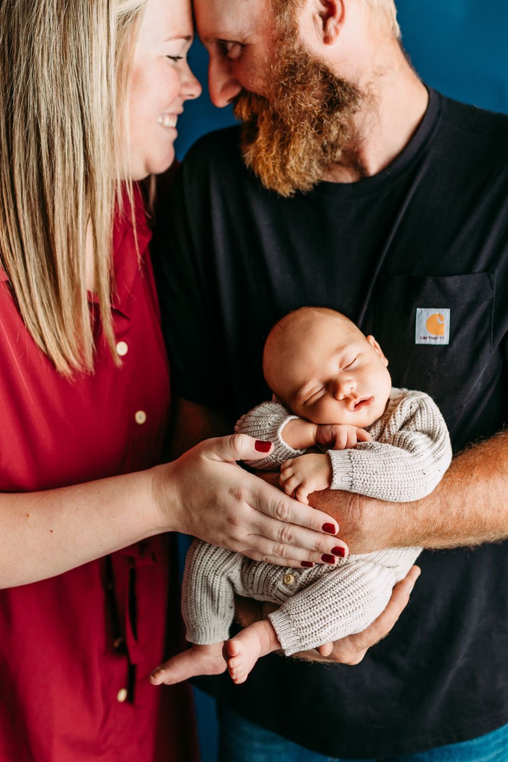 A series of tender moments with a sleeping newborn cradled between two parents against a blue backdrop.