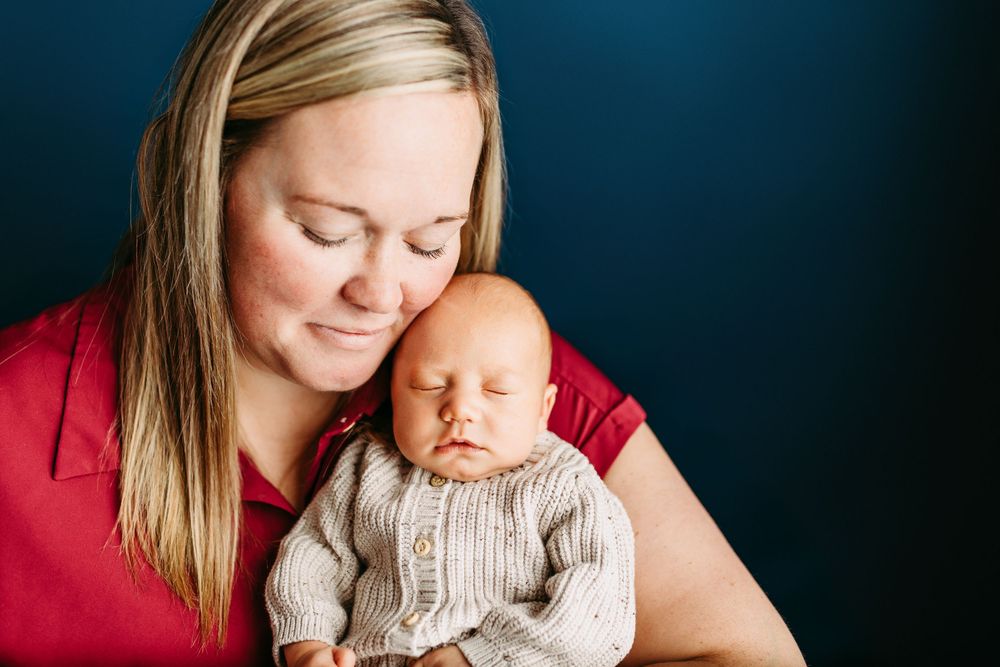 Tender portrait of parent and newborn on dark backdrop with loving expression and emotional connection.