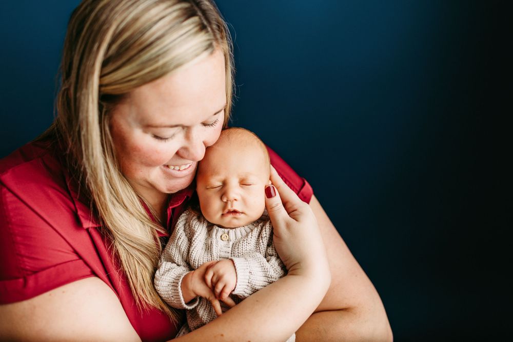 Tender bonding moment between parent and baby as they cuddle close together in front of a navy blue backdrop.