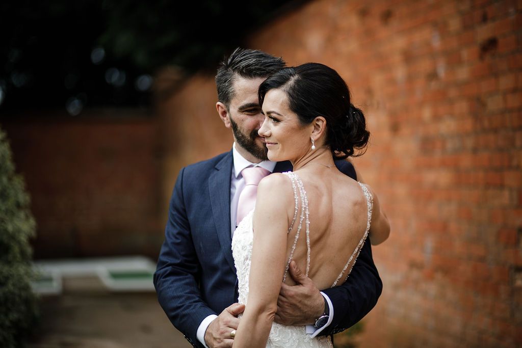 Couple sharing an intimate wedding moment with romantic lighting against a red-brick wall at Kelham House