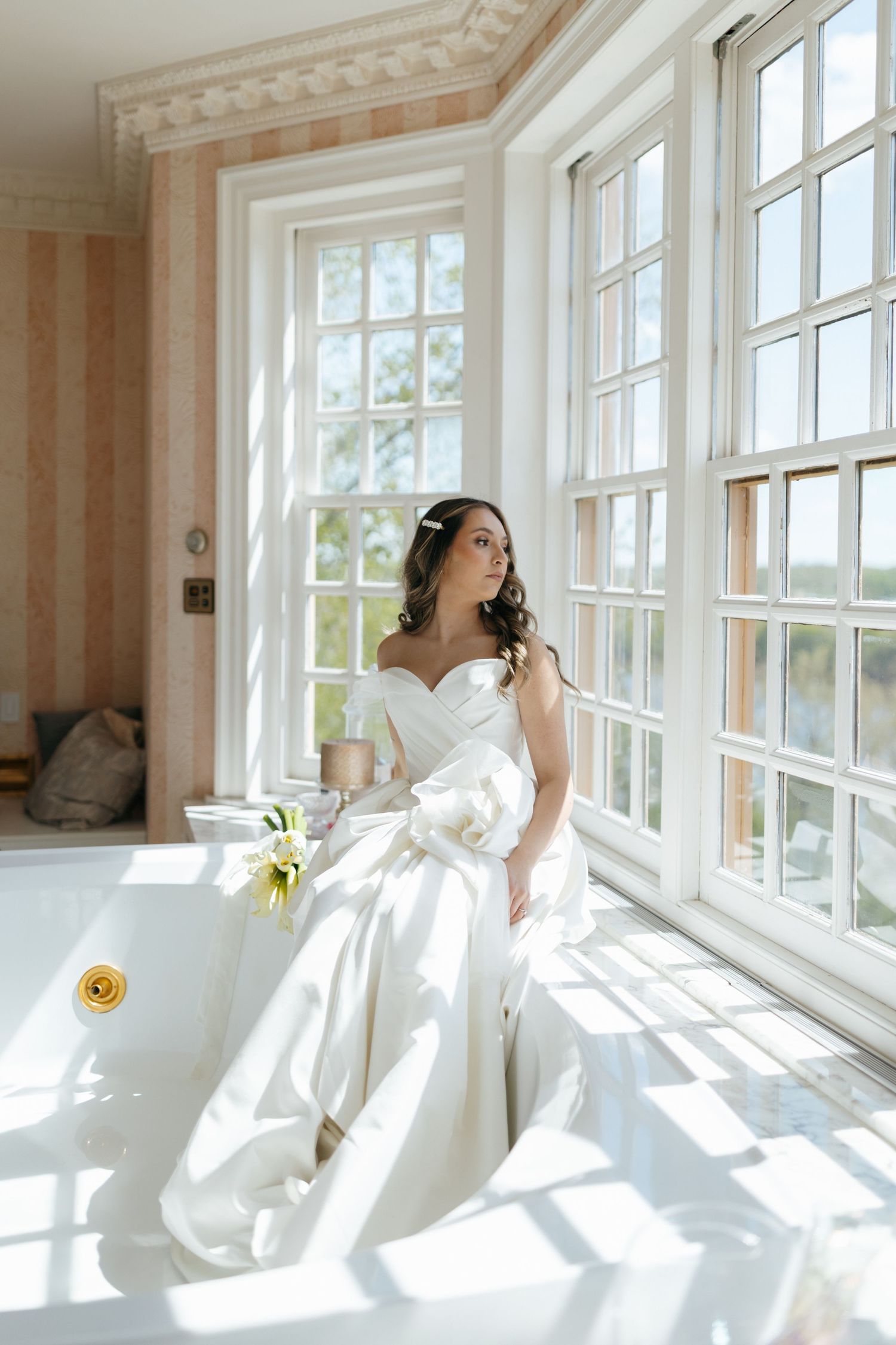 A romantic wedding couple embraces in a sunlit forest setting with a flowing white veil during golden hour.