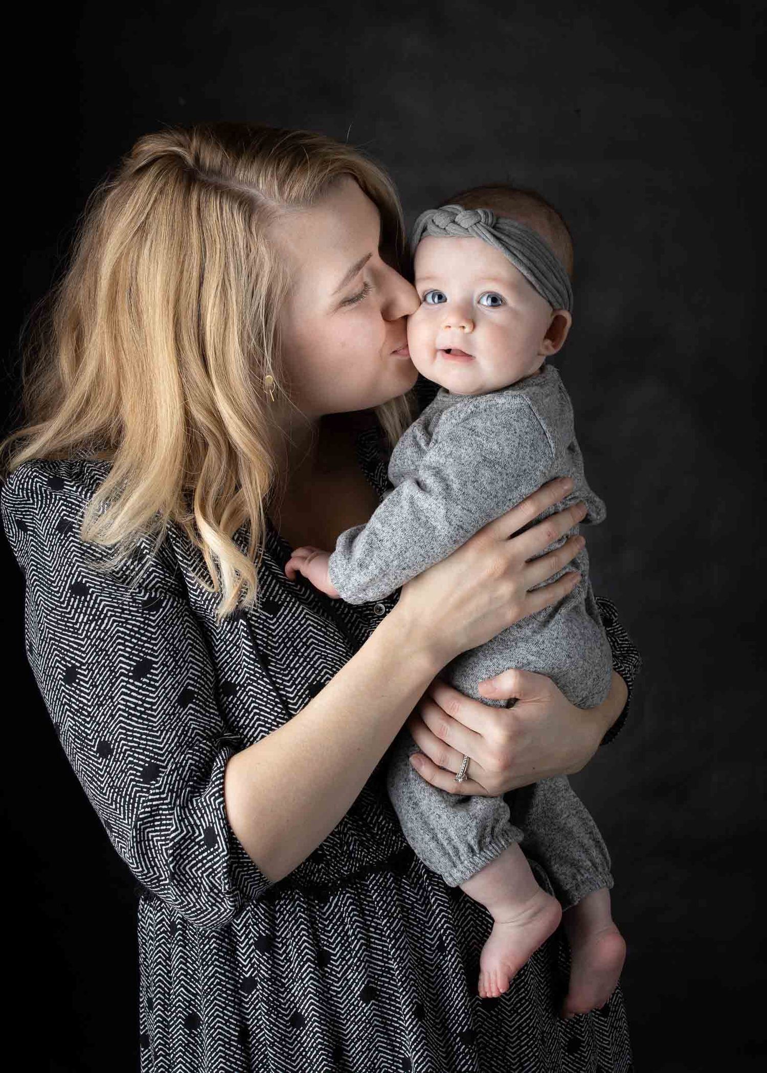 Mother holding and kissing her baby during a studio portrait session.