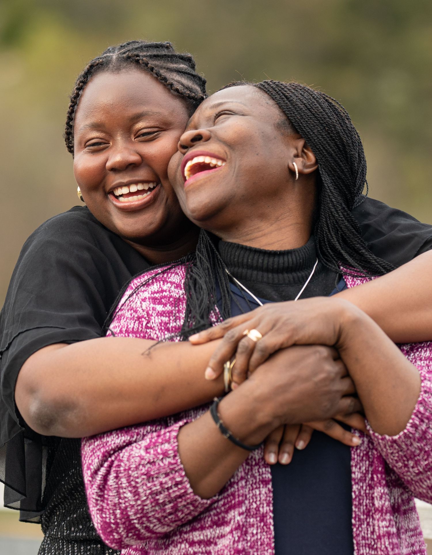 Two Black women laughing and embracing joyfully outdoors in a heartwarming portrait. Family Photo by Xenophon Photography in Maine.