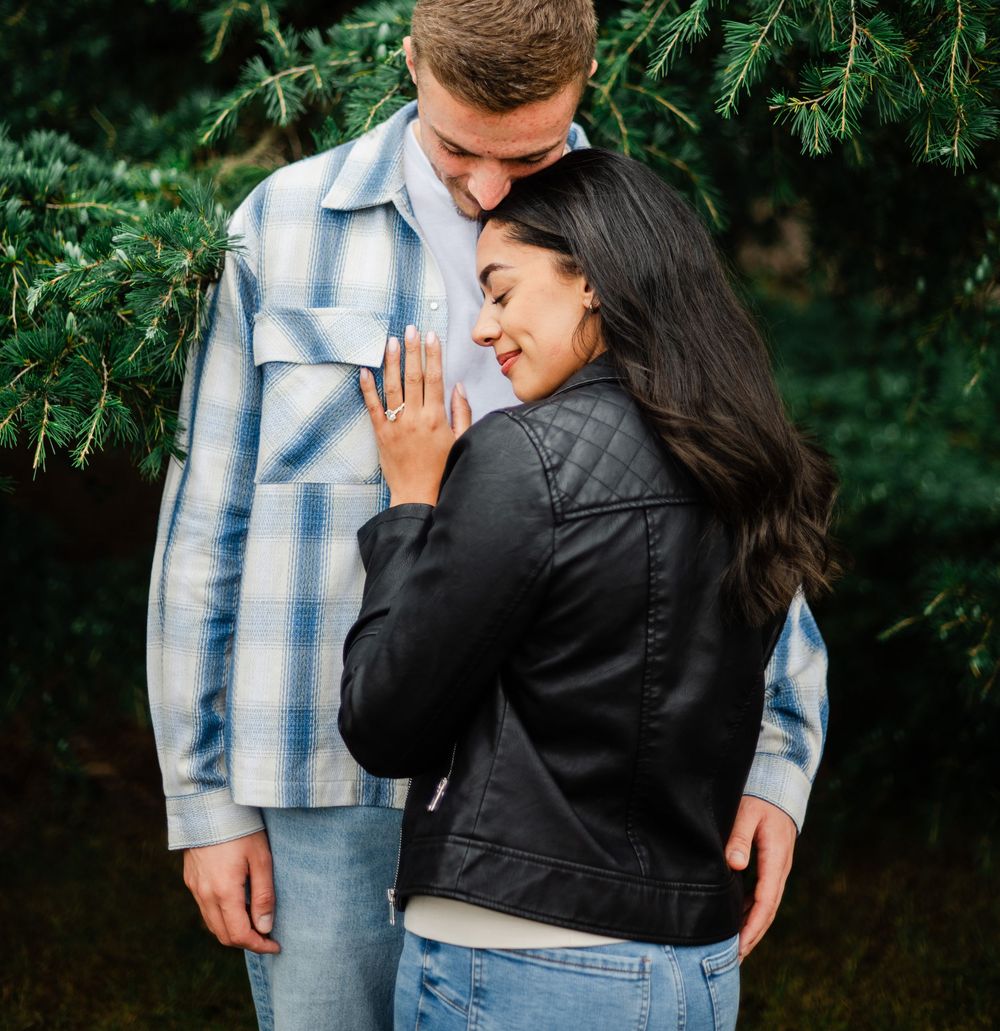 A romantic moment captured against lush green foliage during an outdoor engagement photoshoot.