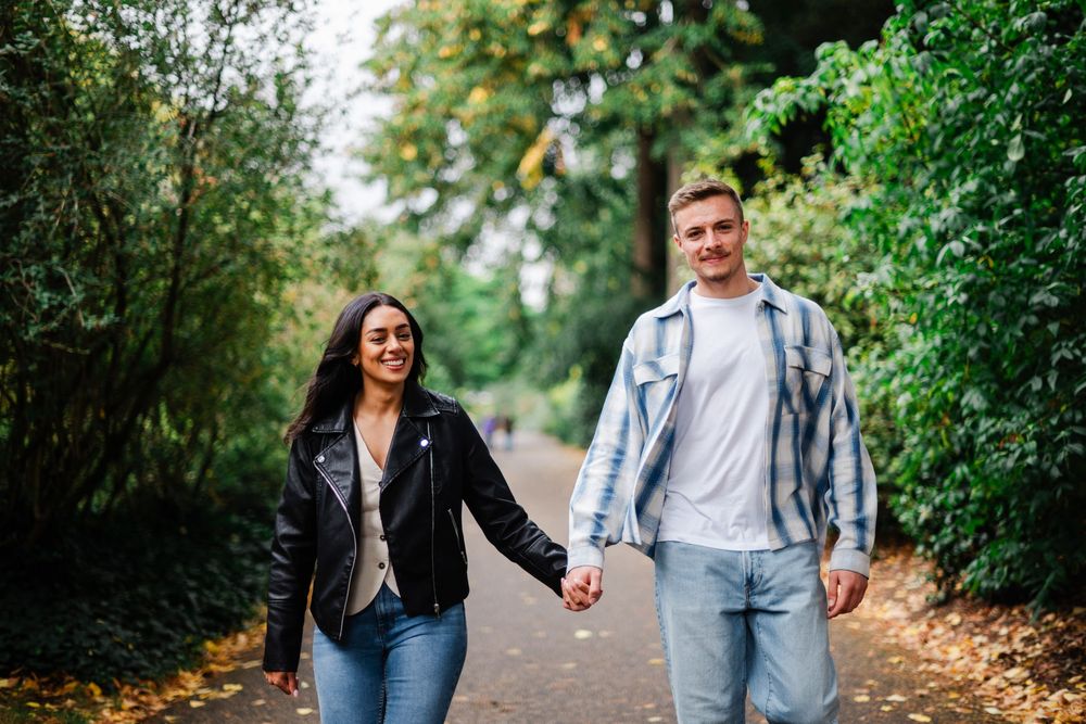 A couple walking together and laughing on a lush tree-lined path during autumn.