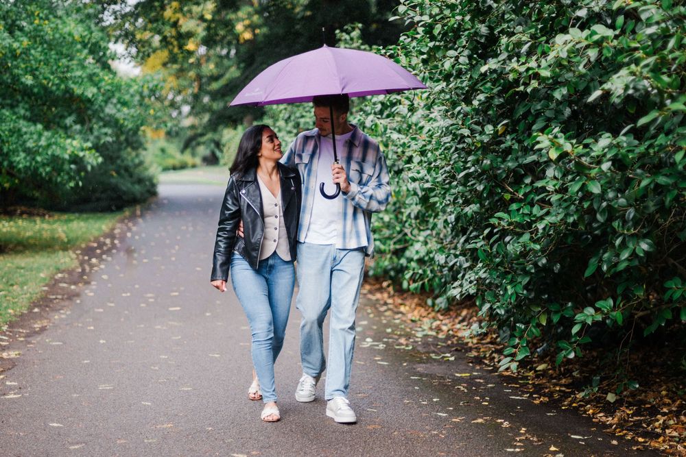Engagement photoshoot at Kew Gardens after proposal, with couple walking hand in hand under umbrellas.