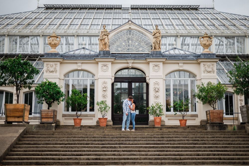 Historical Victorian greenhouse exterior with stone steps, potted plants, and elegant arched windows and doorways.