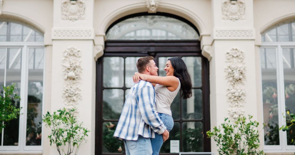 A couple embracing in front of an elegant historic building entrance with decorative stone carvings.