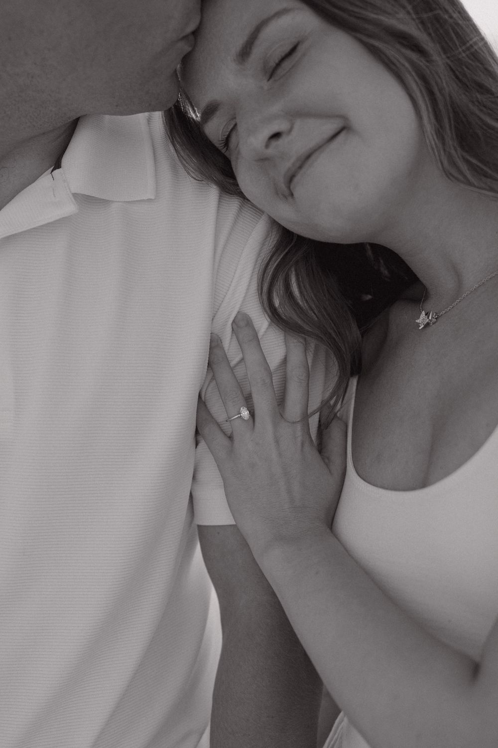 Black and white intimate portrait showing a tender embrace with a content expression and white clothing.