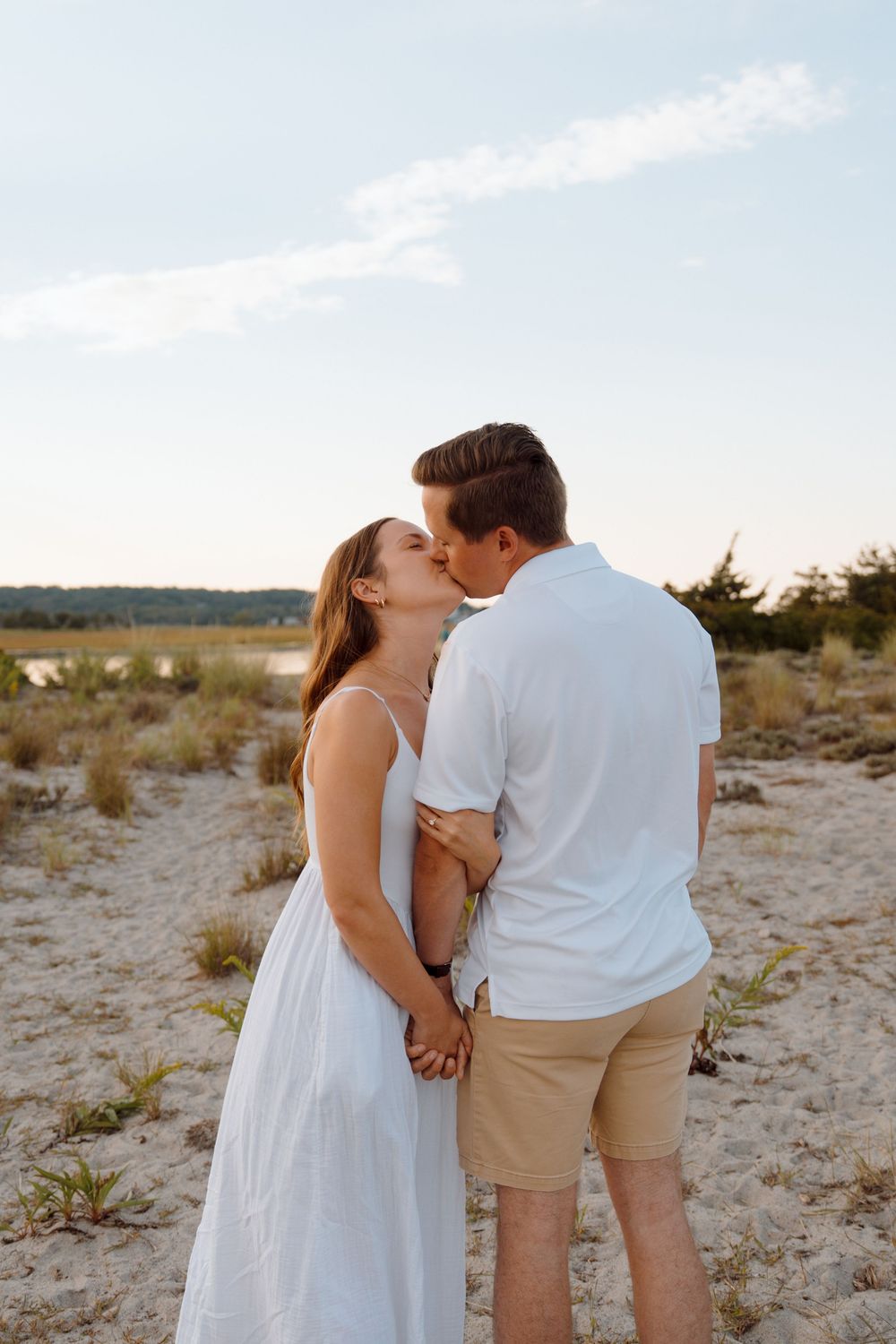 Romantic couple in white and khaki outfits stroll along sandy beach dunes at sunset in sequence of loving poses.