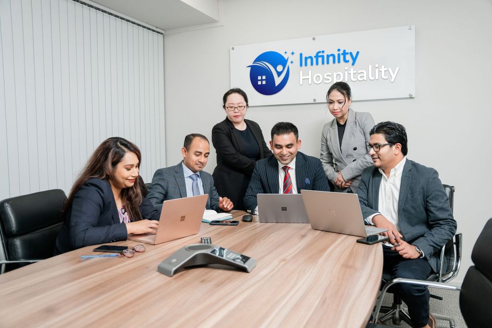 Business professionals meet around a wooden conference table in a modern office setting with corporate branding visible.