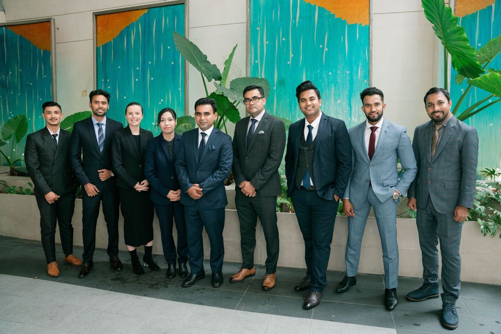 A group of men in formal business attire stand in a line against a turquoise and orange decorated wall.