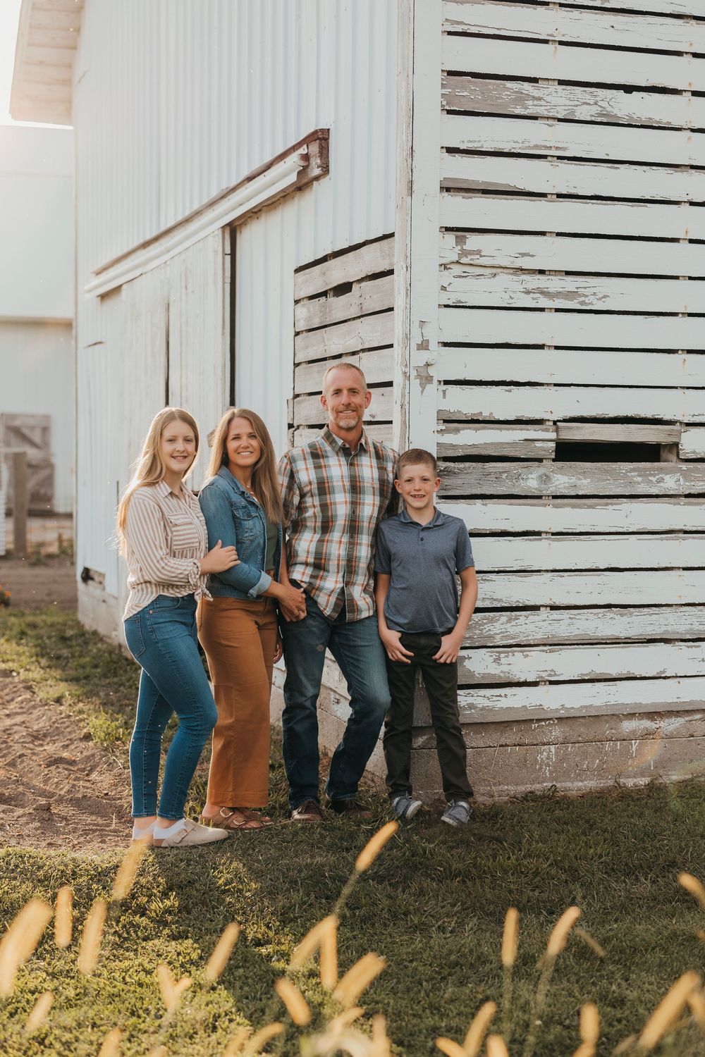 A family sits together on wooden steps of a rustic white barn during an outdoor photo session.