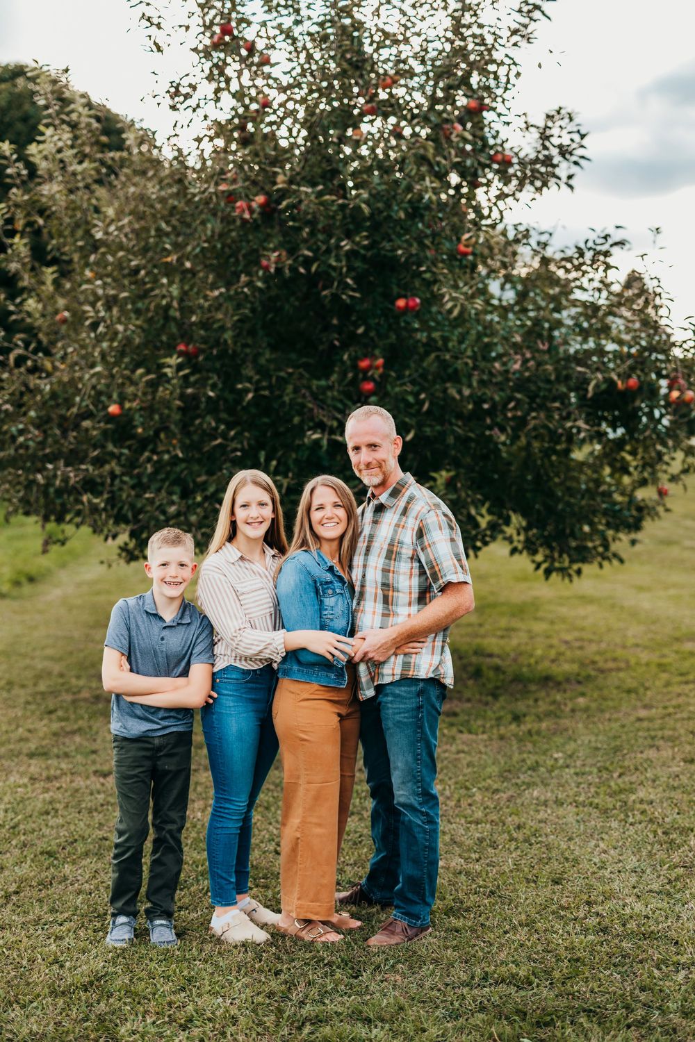 A family stands together near an apple tree on a grassy hillside during a sunny autumn day.