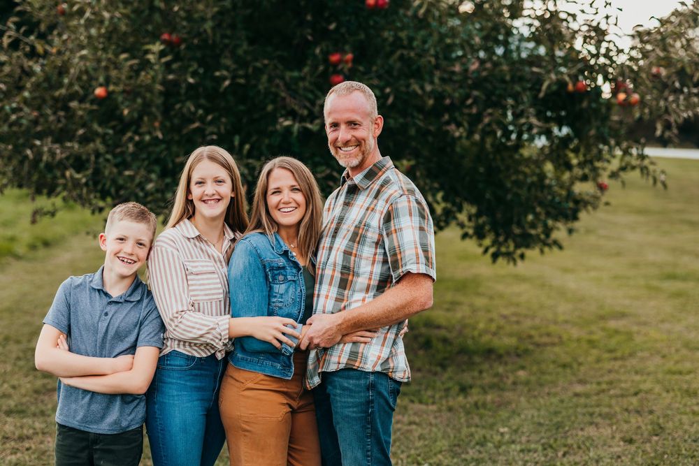 A family shares joyful moments together in a casual outdoor photo session at an orchard or park.